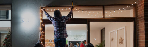 Happy Latin American family decorating the house for Christmas and hanging lights on the door